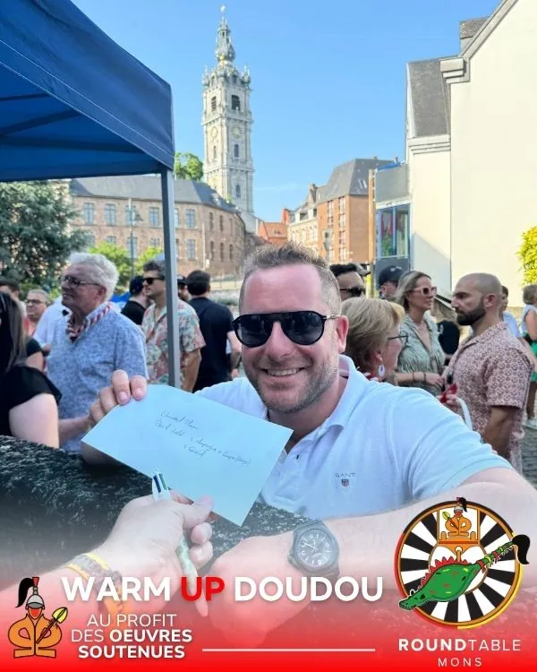 Remise d'une invitation partenaire lors du Warmup Doudou, beffroi de Mons en fond